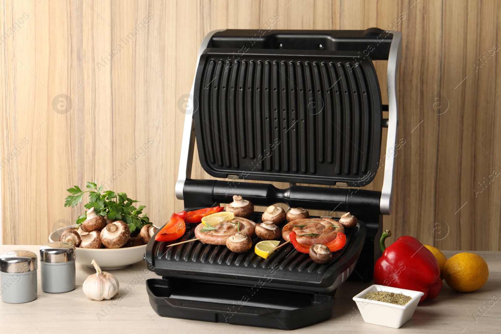 Photo of Electric grill with homemade sausages, vegetables and spices on wooden table