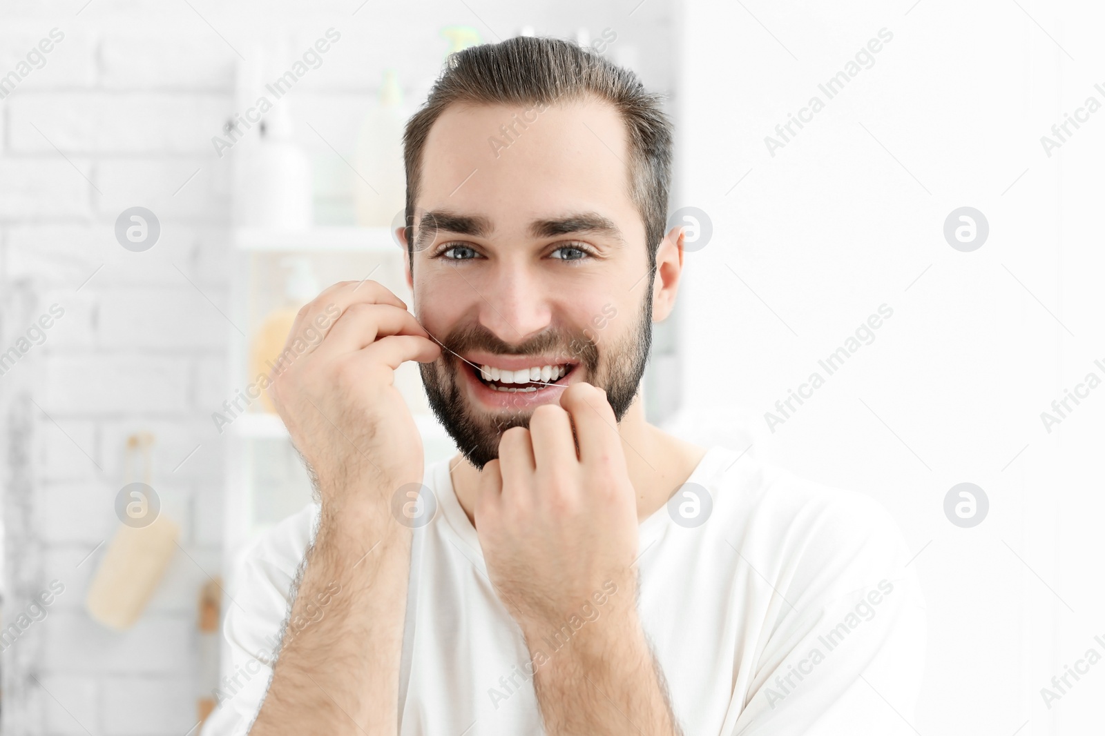 Photo of Young man flossing his teeth indoors