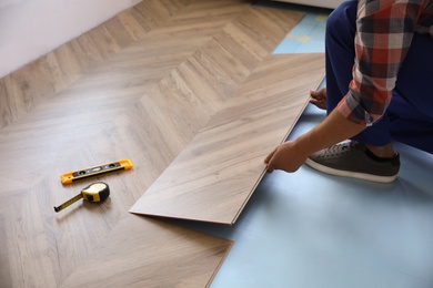 Photo of Worker installing laminated wooden floor indoors, closeup