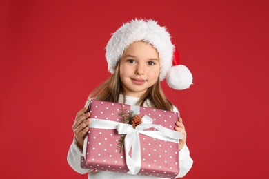 Photo of Cute child in Santa hat with Christmas gift on red background