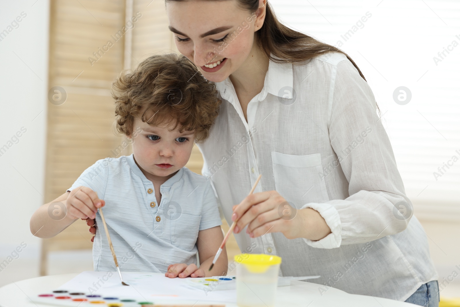 Photo of Mother and her little son painting with watercolor at home, closeup