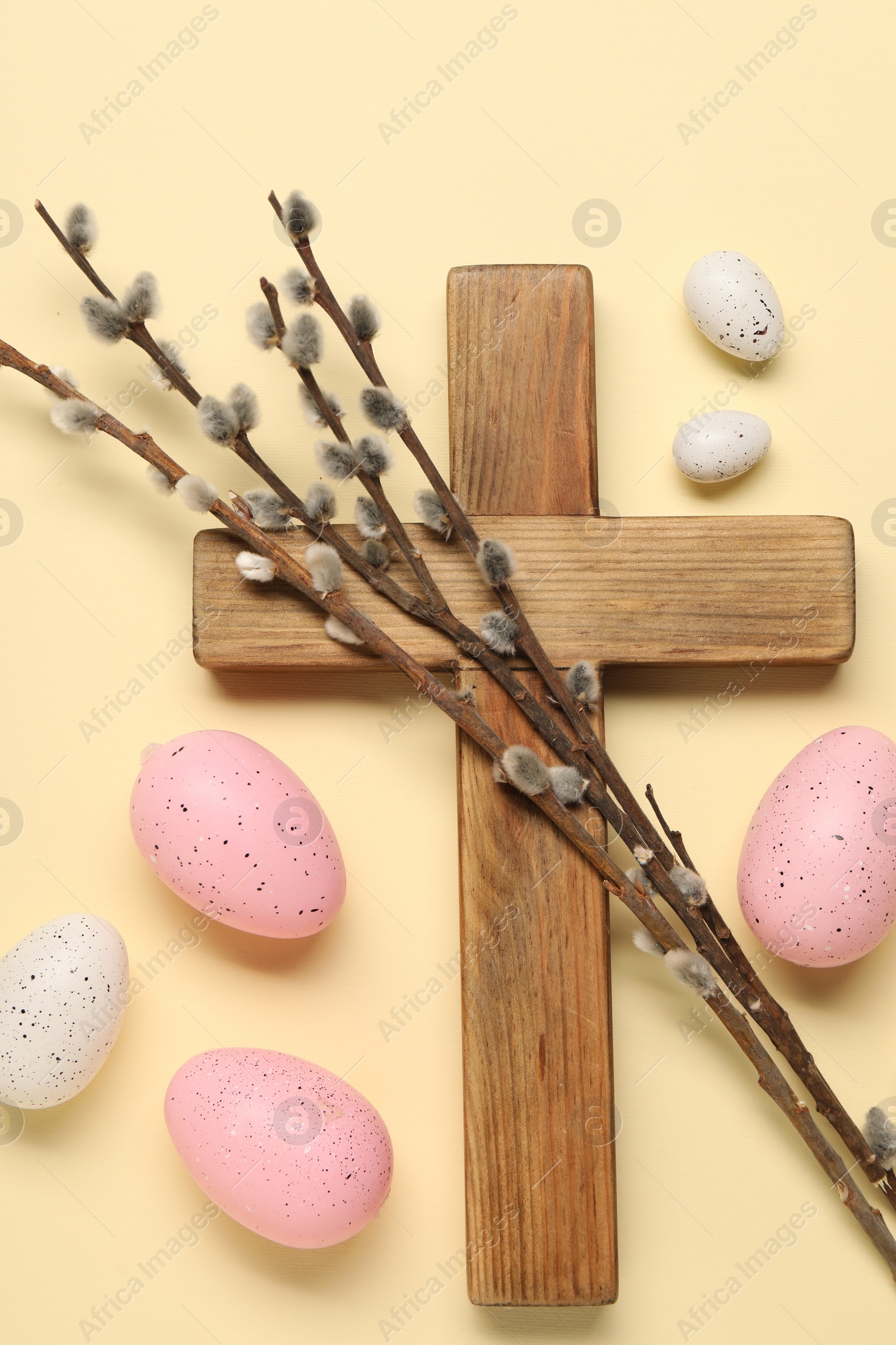 Photo of Wooden cross, painted Easter eggs and willow branches on beige background, flat lay