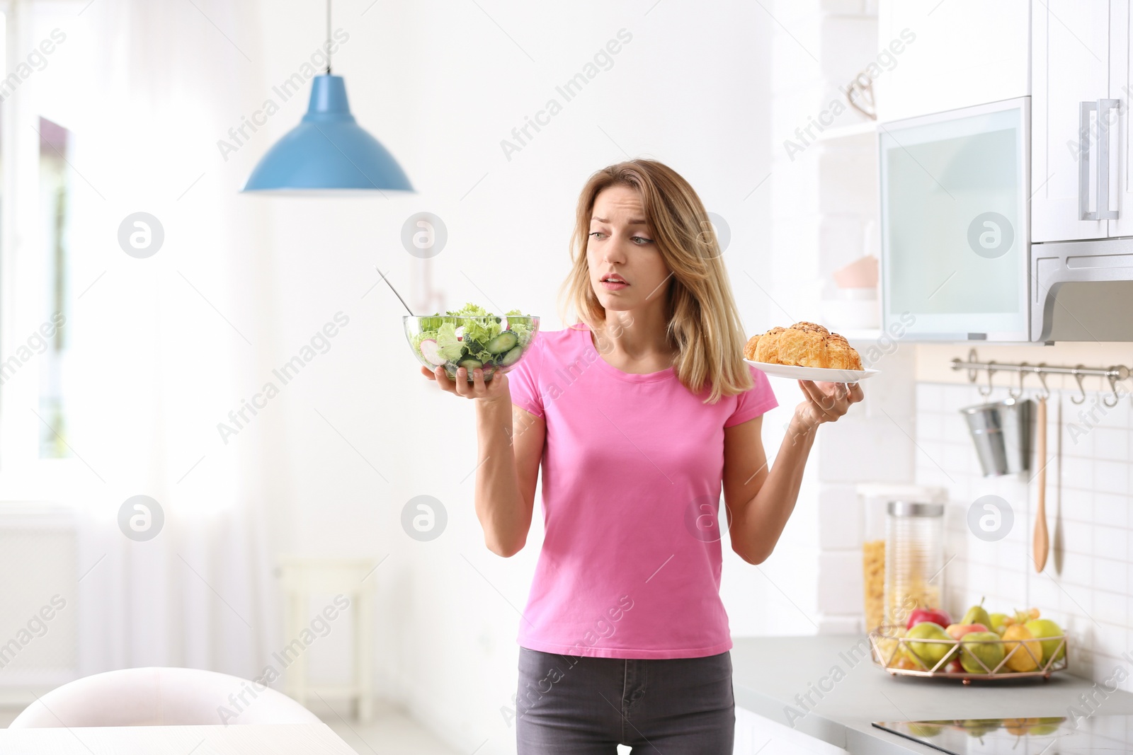 Photo of Woman choosing between vegetable salad and dessert in kitchen. Healthy diet