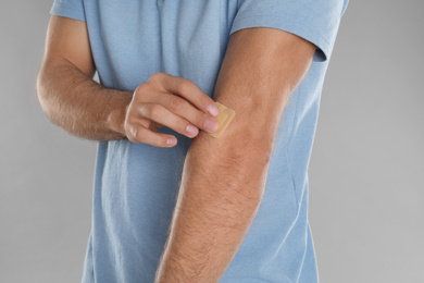 Photo of Man putting sticking plaster onto arm against light grey background, closeup