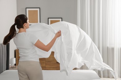 Photo of Young woman changing bed linens at home
