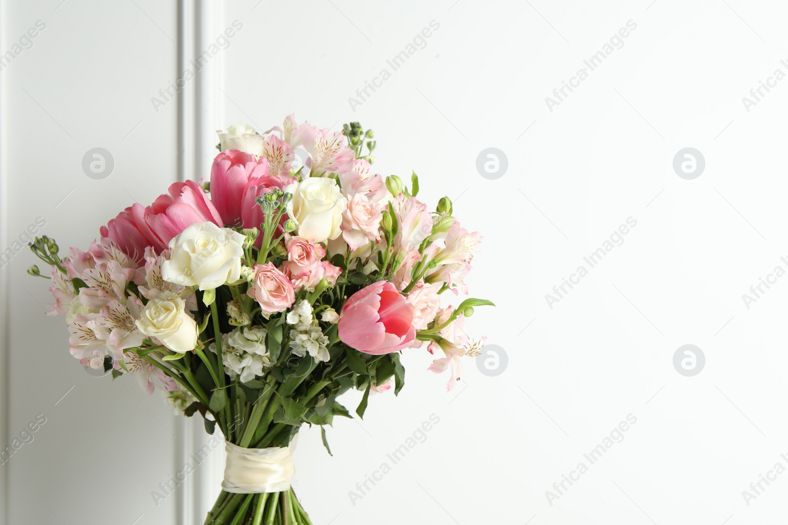 Photo of Beautiful bouquet of fresh flowers near white wall. Space for text