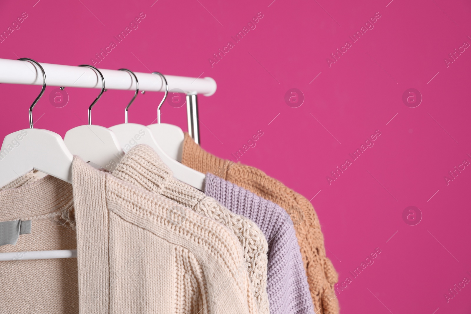 Photo of Collection of warm sweaters hanging on rack against color background. Space for text