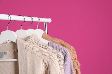 Collection of warm sweaters hanging on rack against color background. Space for text