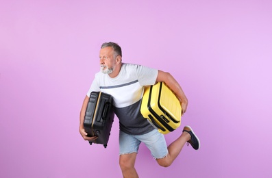 Photo of Senior man with suitcases running on color background. Vacation travel