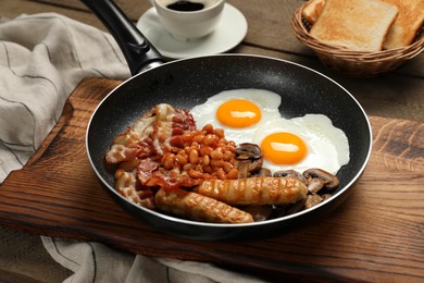 Photo of Frying pan with cooked traditional English breakfast on wooden table