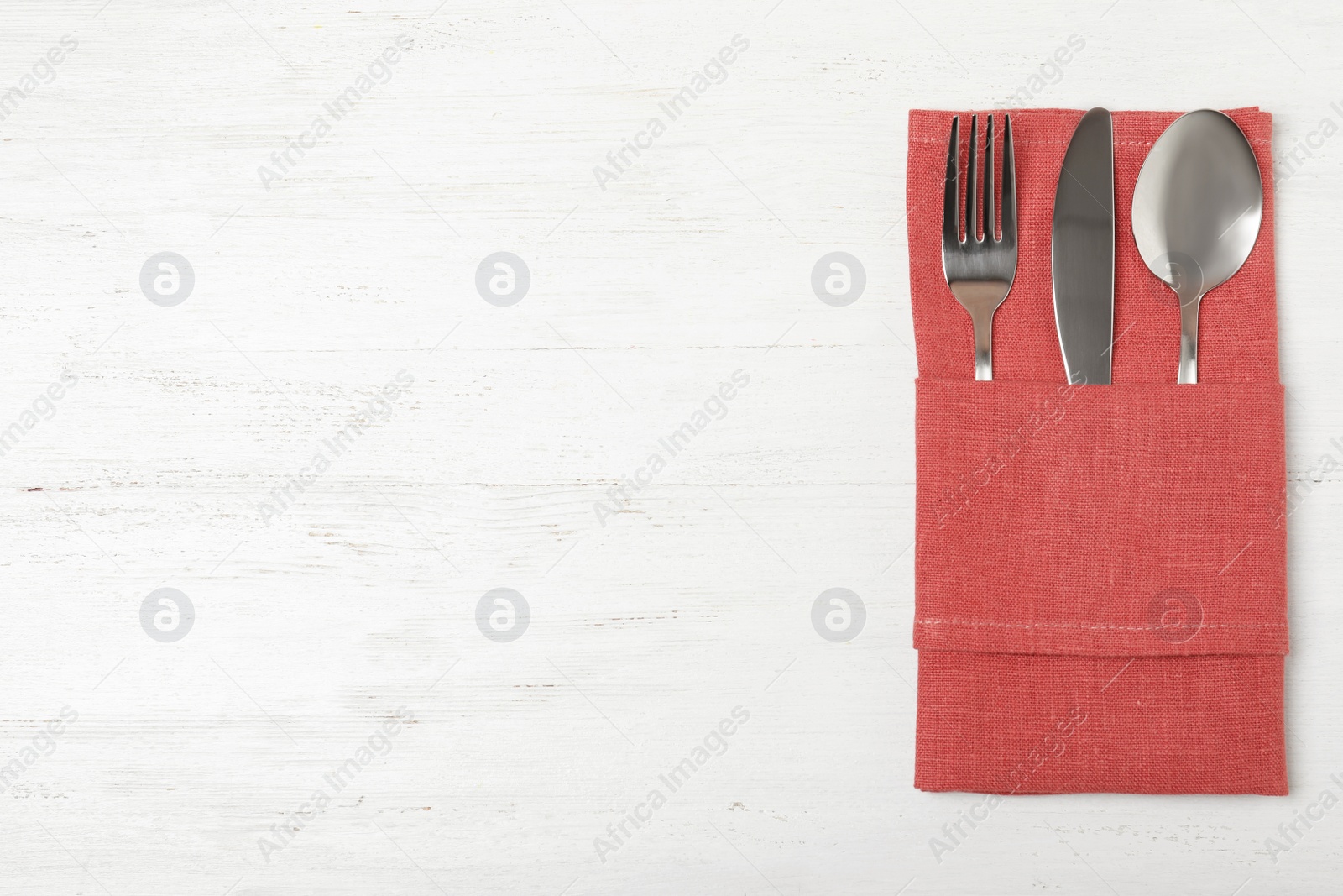 Photo of Folded napkin with fork, spoon and knife on white wooden background, top view. Space for text