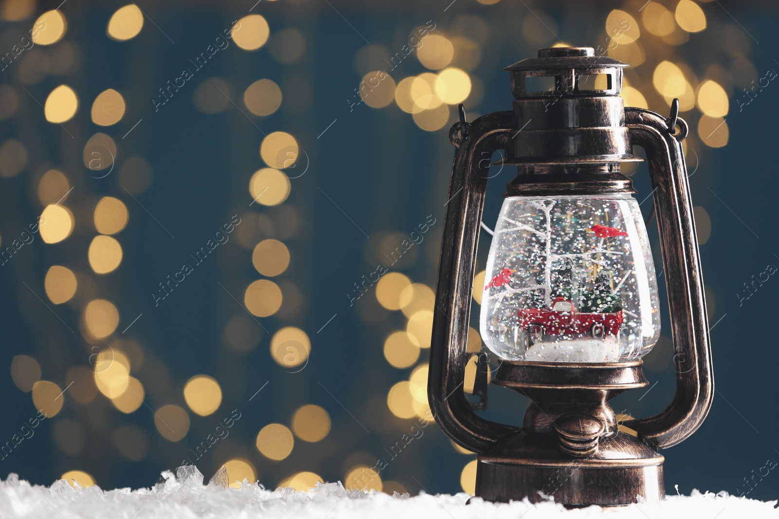Photo of Snow globe in vintage lantern against blurred Christmas lights. Space for text