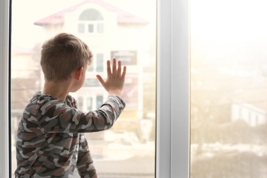 Photo of Lonely little boy near window indoors. Child autism