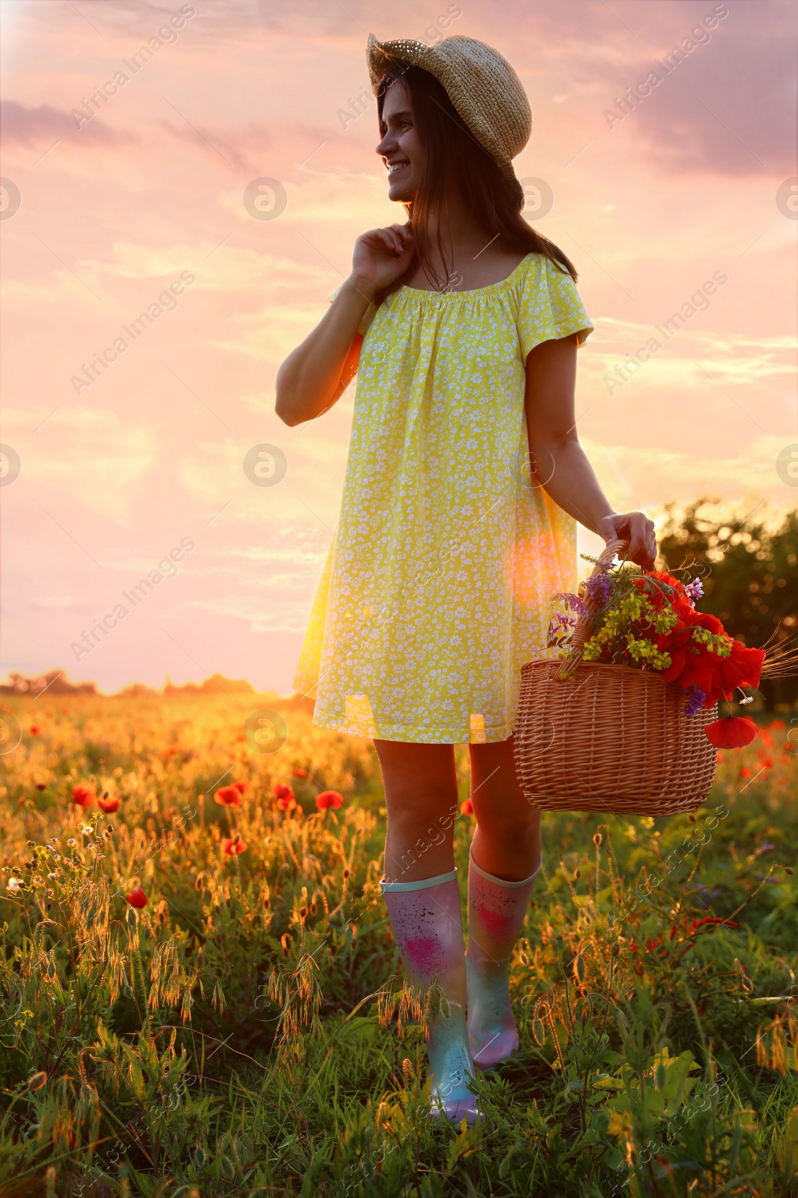 Photo of Woman with basket of poppies and wildflowers in beautiful field at sunset