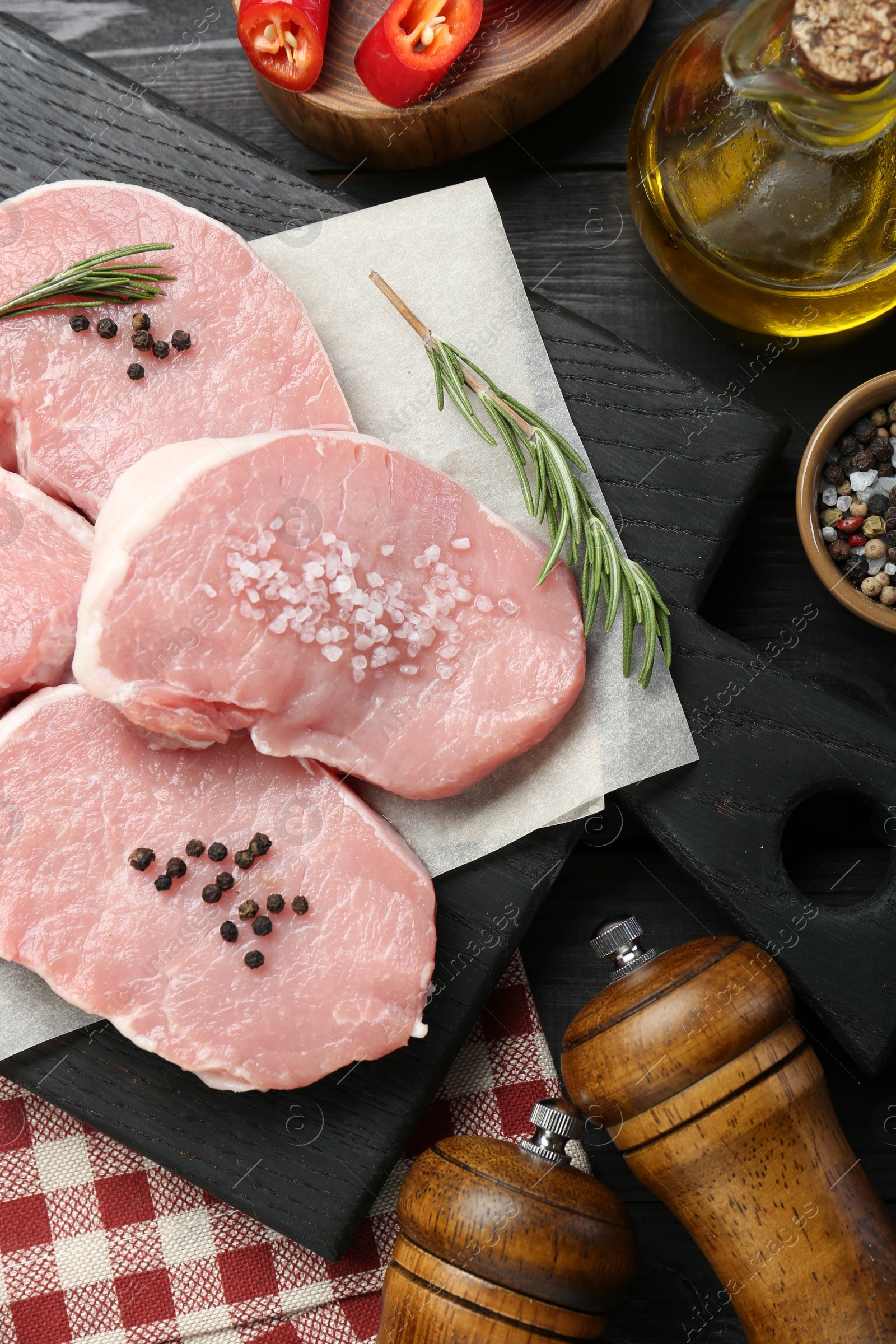 Photo of Pieces of raw pork meat and spices on black wooden table, flat lay