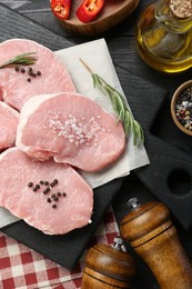 Photo of Pieces of raw pork meat and spices on black wooden table, flat lay