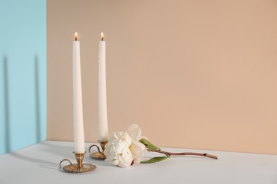Photo of Elegant candlesticks with burning candles and flower on white table