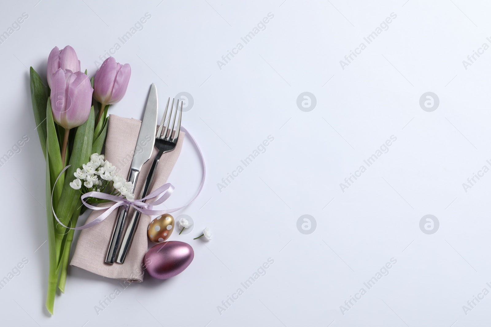 Photo of Cutlery set, Easter eggs and beautiful flowers on white background, flat lay with space for text. Festive table setting