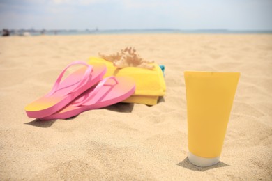 Photo of Tube of sunscreen, beach accessories and starfish on sand, selective focus. Sun protection care