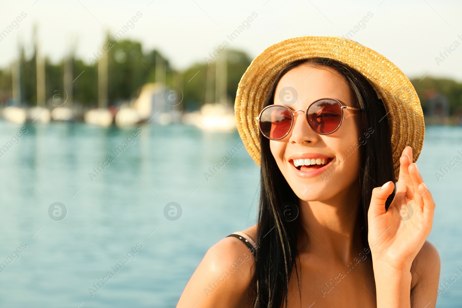 Photo of Beautiful young woman wearing stylish sunglasses near river. Space for text