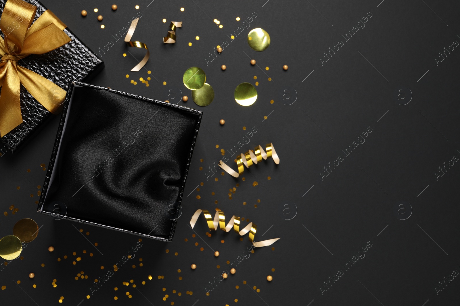 Photo of Open gift box, confetti and streamers on black  background, flat lay. Space for text