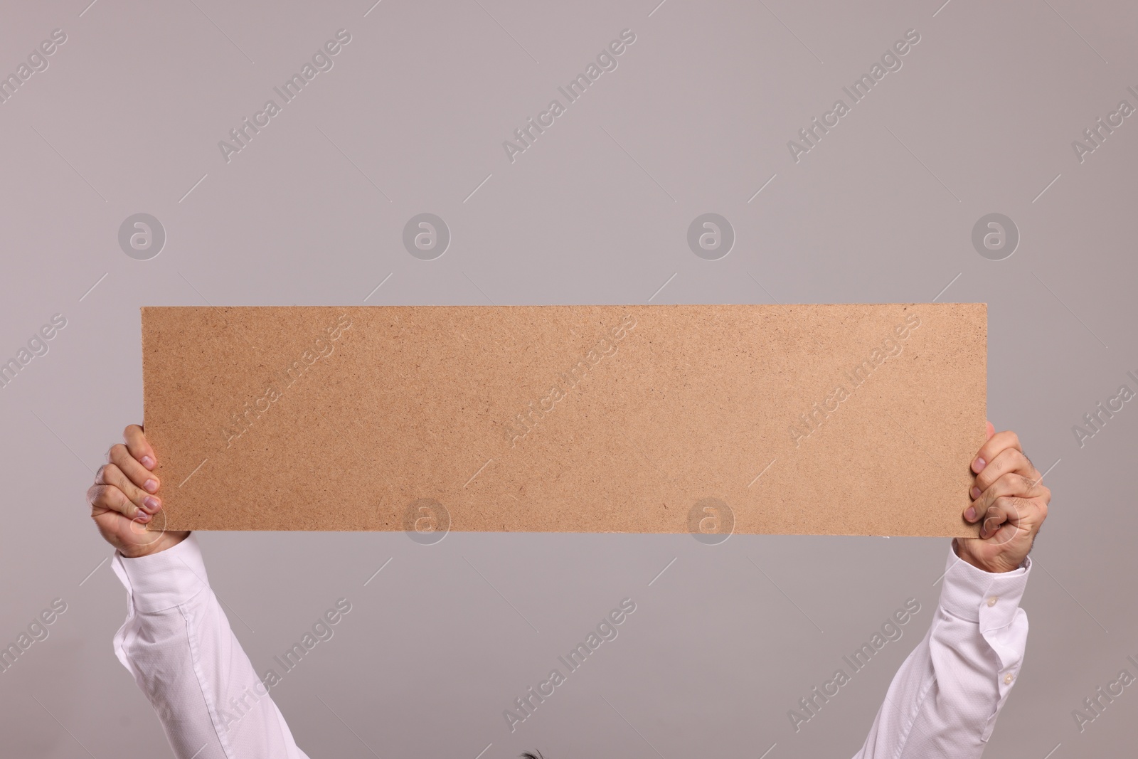 Photo of Man holding blank cardboard banner on light grey background, closeup. Space for text