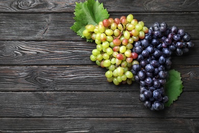 Photo of Different fresh ripe juicy grapes and space for text on wooden table, top view