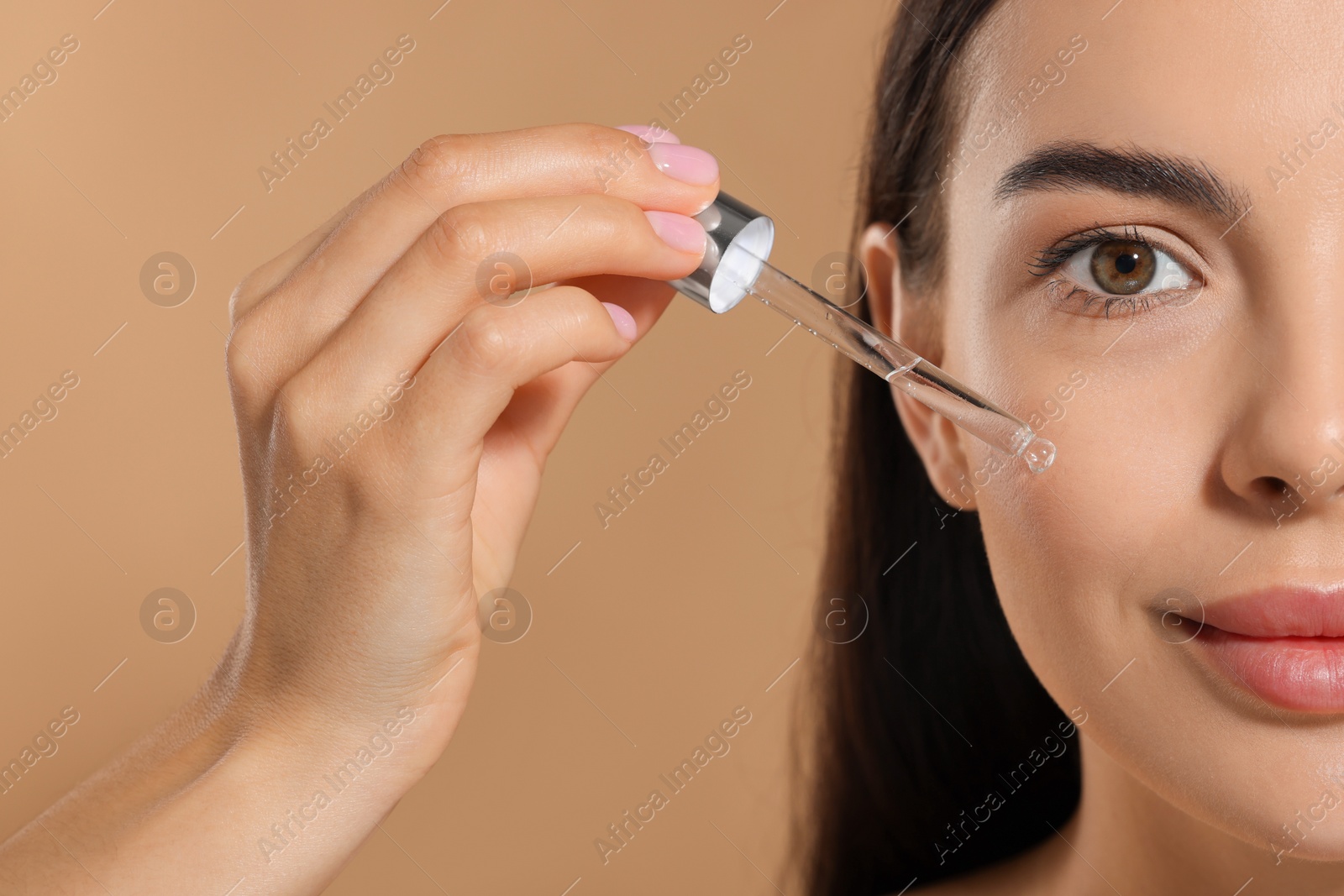 Photo of Beautiful young woman applying serum onto her face on beige background, closeup