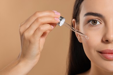 Photo of Beautiful young woman applying serum onto her face on beige background, closeup