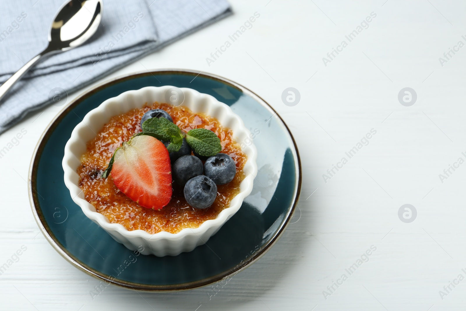Photo of Delicious creme brulee with berries and mint in bowl on white wooden table, closeup. Space for text