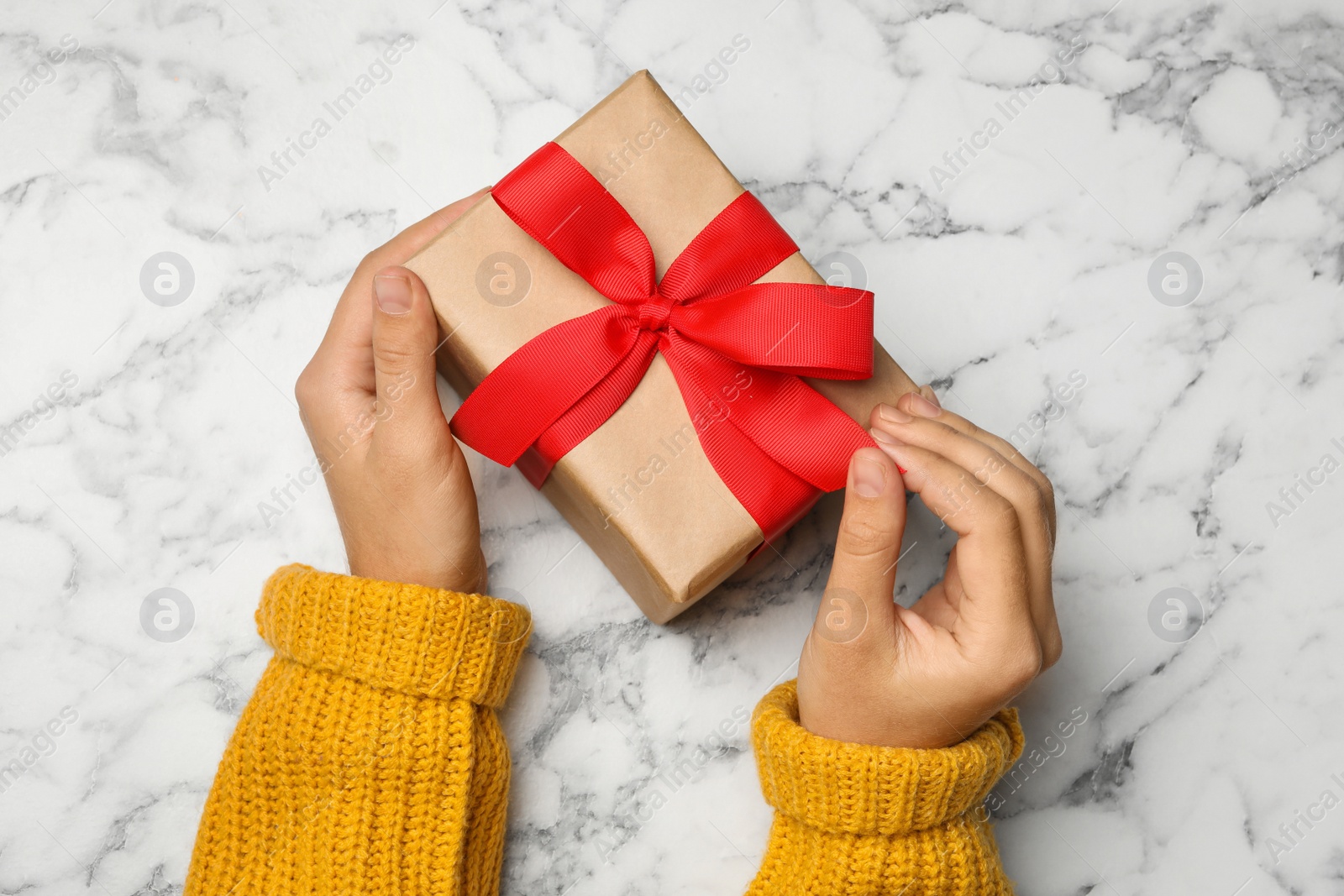 Photo of Young woman holding Christmas gift on white marble background, top view