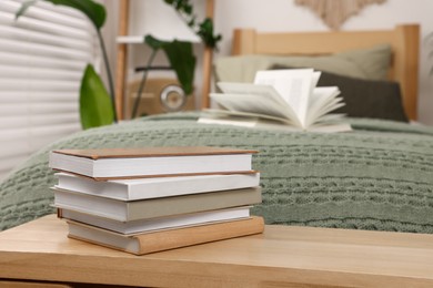 Stacked hardcover books on wooden table near bed indoors. Space for text