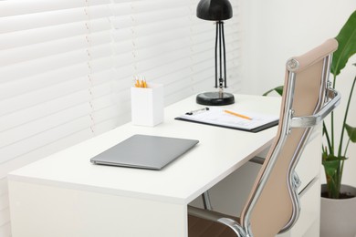 Photo of Doctor's workplace. Chair, laptop and clipboard on white table in clinic