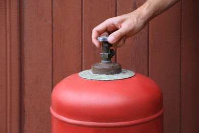 Man opening red gas cylinder near brown wooden wall, closeup