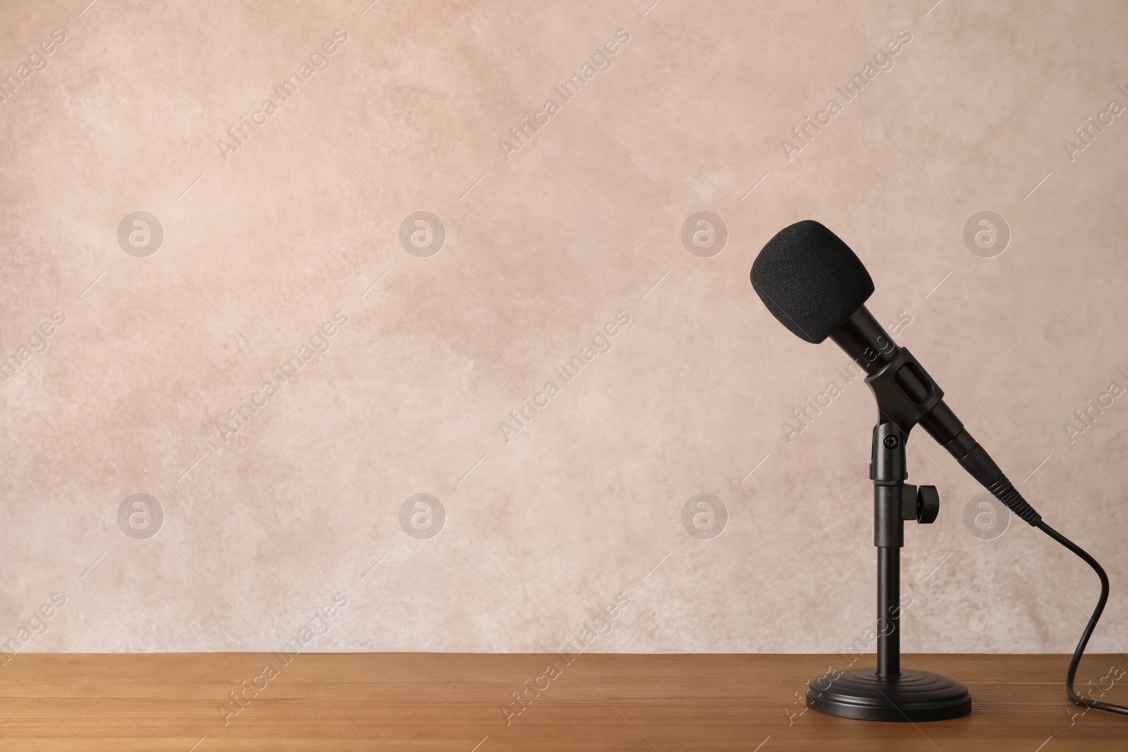 Photo of Modern microphone on table against color background. Space for text