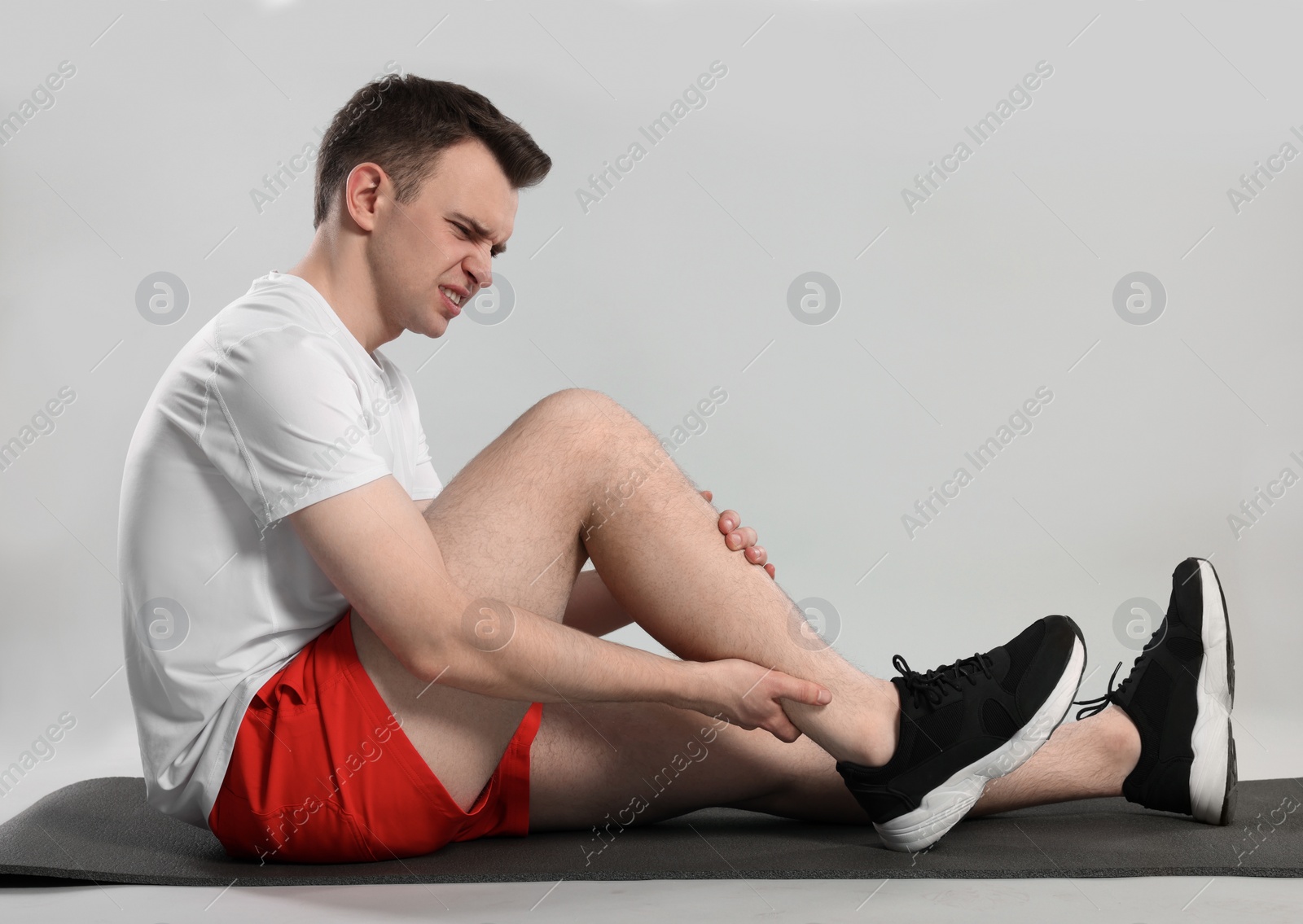 Photo of Man suffering from leg pain on mat against grey background