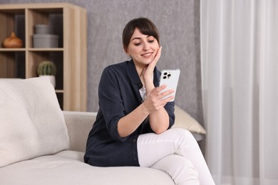 Photo of Beautiful young housewife using smartphone on sofa at home