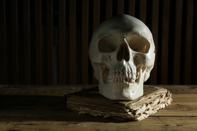 Human skull and old book on wooden table, space for text