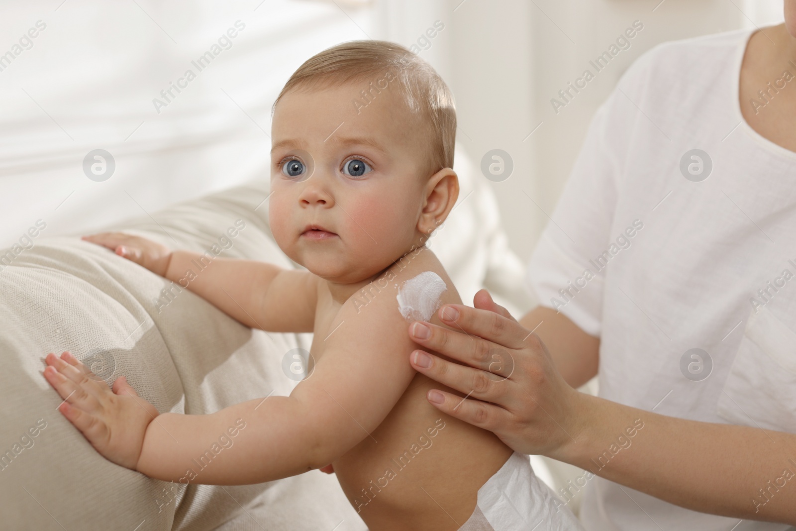 Photo of Mother applying body cream on her little baby at home, closeup