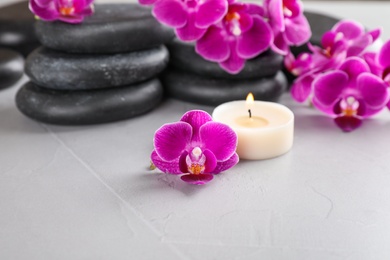 Photo of Spa stones, orchid flowers and candle on grey background