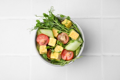 Bowl of tasty salad with tofu and vegetables on white tiled table, top view