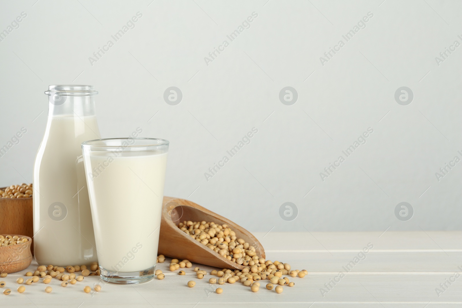 Photo of Fresh soy milk and grains on white wooden table. Space for text