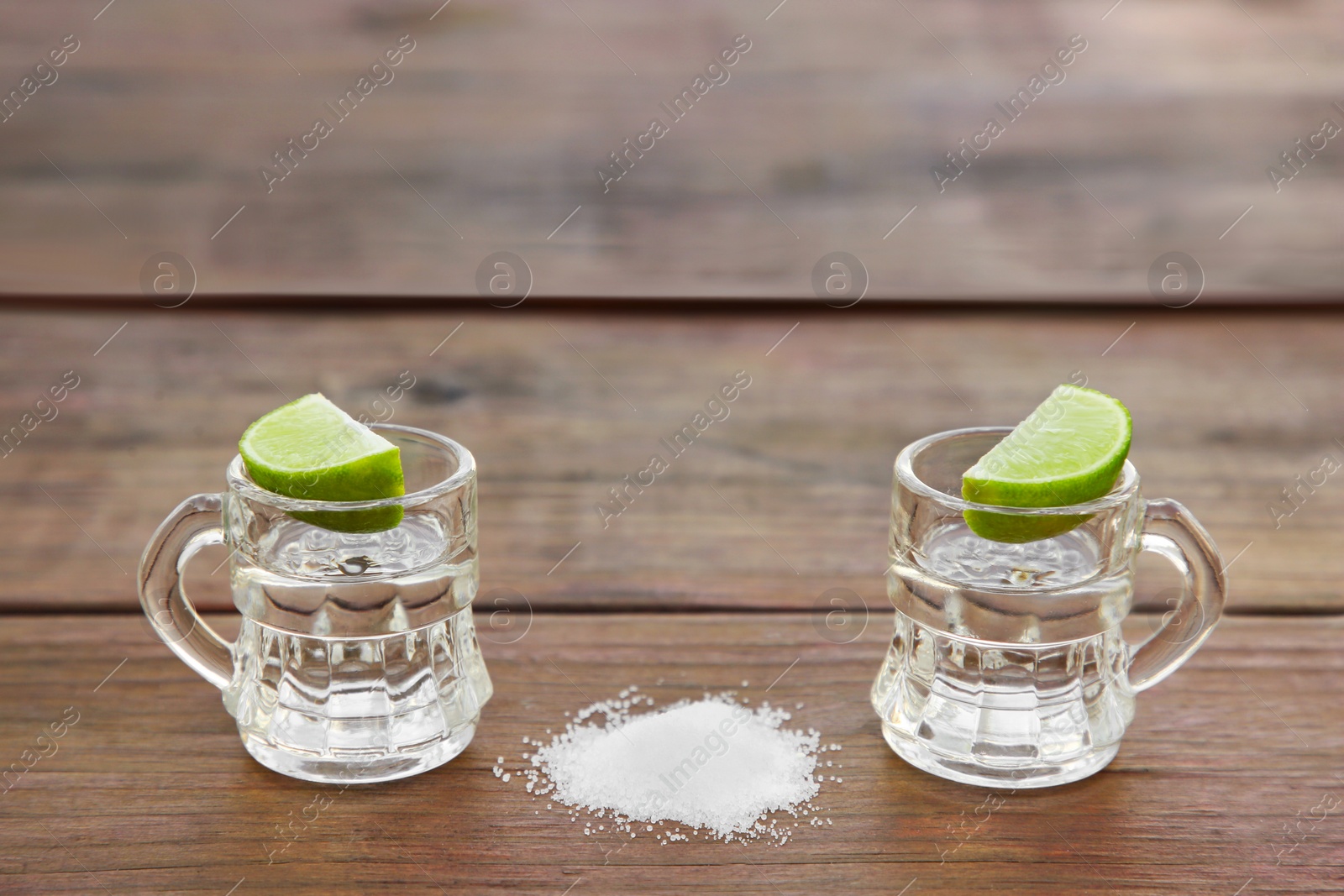 Photo of Mexican tequila shots with lime slices and salt on wooden table, space for text. Drink made from agave