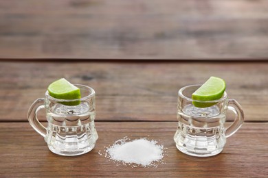 Mexican tequila shots with lime slices and salt on wooden table, space for text. Drink made from agave
