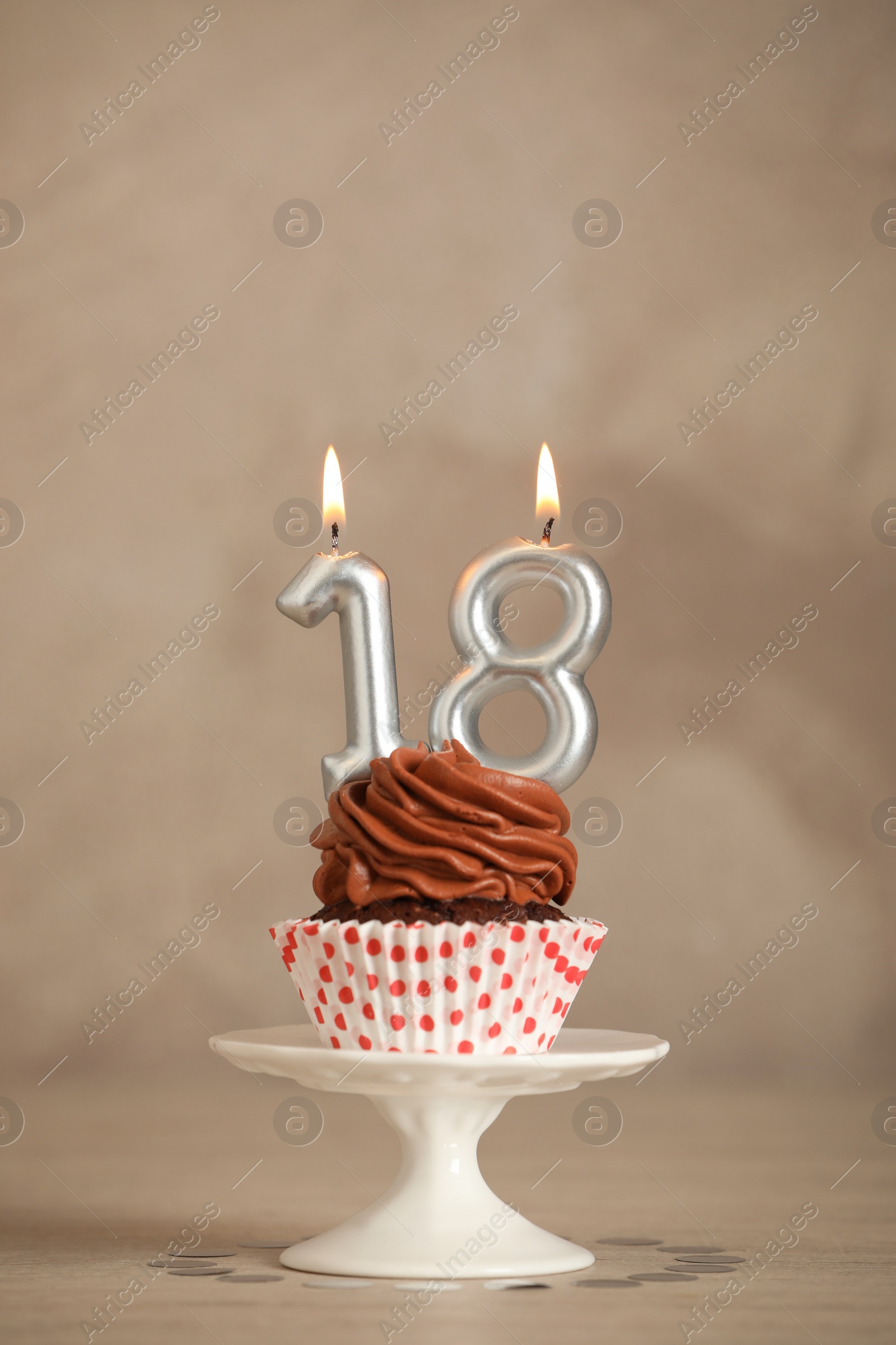 Photo of 18th birthday. Delicious cupcake with number shaped candles for coming of age party on beige table