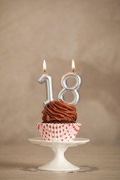 Photo of 18th birthday. Delicious cupcake with number shaped candles for coming of age party on beige table