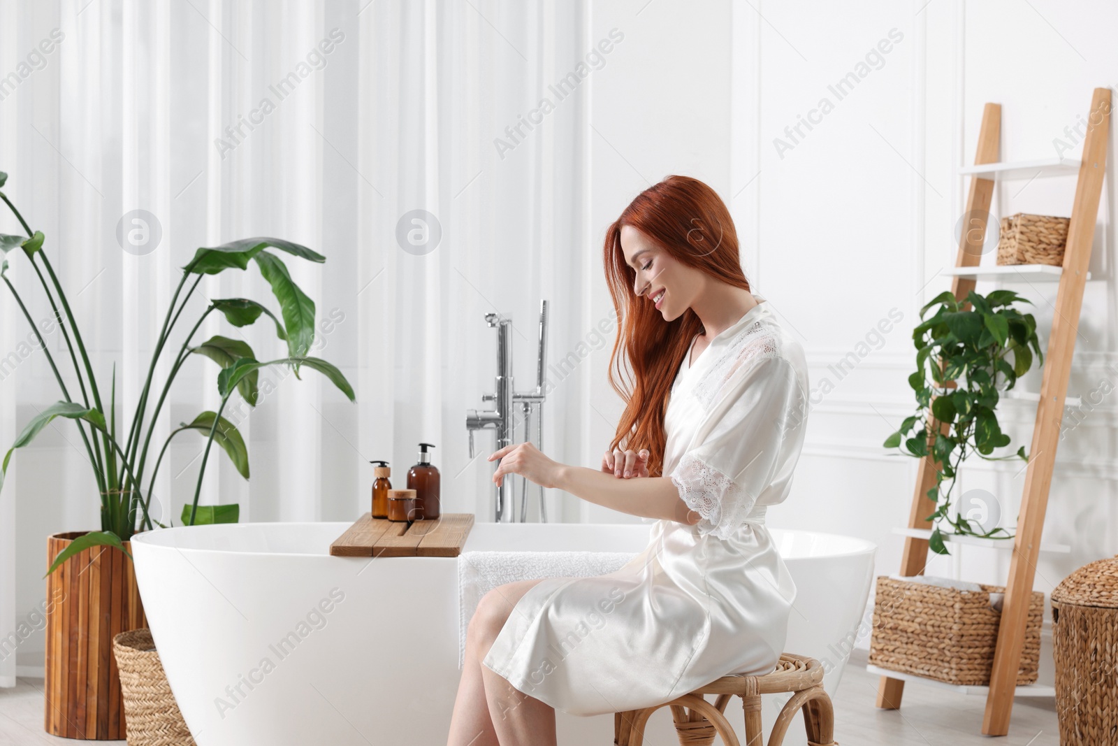 Photo of Beautiful young woman touching her smooth arms in bathroom, space for text