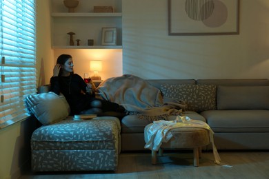 Woman with glass of wine resting on couch in room at night