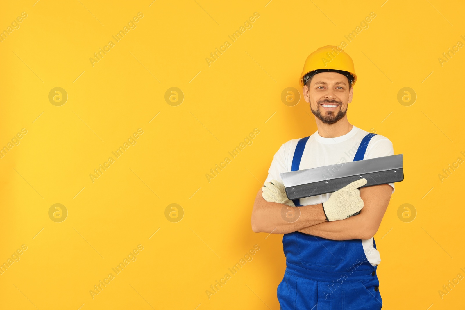 Photo of Professional worker with putty knife in hard hat on orange background, space for text