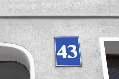 Photo of Plate with house number fourty three on light grey wall outdoors